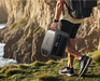 Anker SOLIX C1000 Gen2 1,024Wh | 2,000W Solar Generator + Choose Your Custom Package Person holding a power bank with a scenic background of cliffs and water.