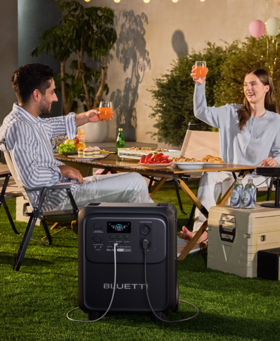BLUETTI Elite 320 Portable Power Station with 1,800 W Output | 3,200 Wh , LCD display and multiple ports on a grass with a couple making a toast at a picnic background www.mygeneratorplus.com 