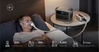 Anker SOLIX C1000 Gen2 1,024Wh | 2,000W Solar Generator + Choose Your Custom Package Man using a CPAP machine in bed with a side table displaying an oxygen concentrator and battery pack.